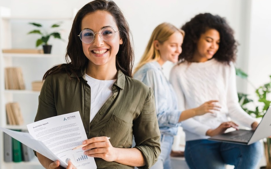 Une jeune femme souriante à lunettes tient un dossier d'évaluation dans un bureau lumineux, représentant une consultante RH Connectt à Nantes ou une intérimaire ravie de son bilan de compétences. En arrière-plan, deux collaboratrices échangent autour d'un ordinateur.